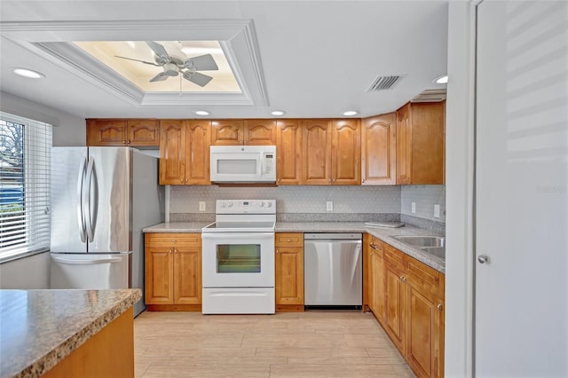 kitchen with visible vents, brown cabinetry, a ceiling fan, a tray ceiling, and stainless steel appliances