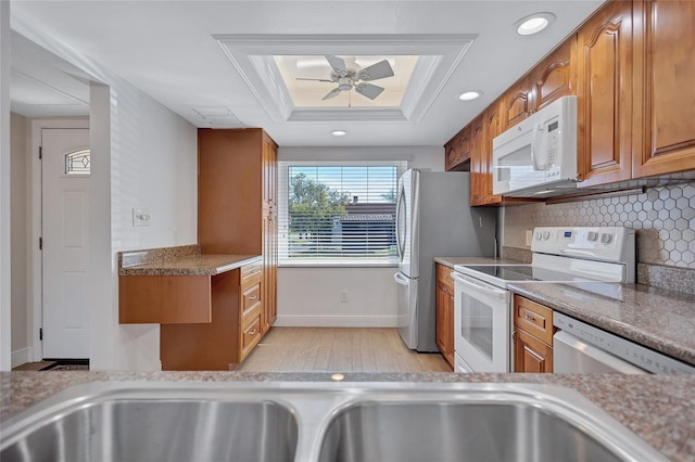 kitchen with a tray ceiling, decorative backsplash, appliances with stainless steel finishes, brown cabinetry, and a ceiling fan