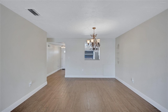 empty room with light wood-style floors, a chandelier, visible vents, and baseboards