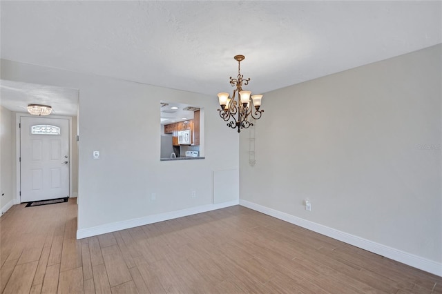 unfurnished room with a chandelier, light wood-style floors, and baseboards