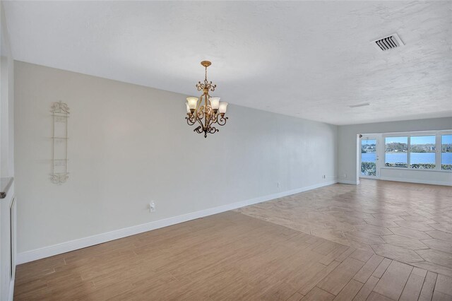 unfurnished room featuring a chandelier, wood finished floors, visible vents, and baseboards