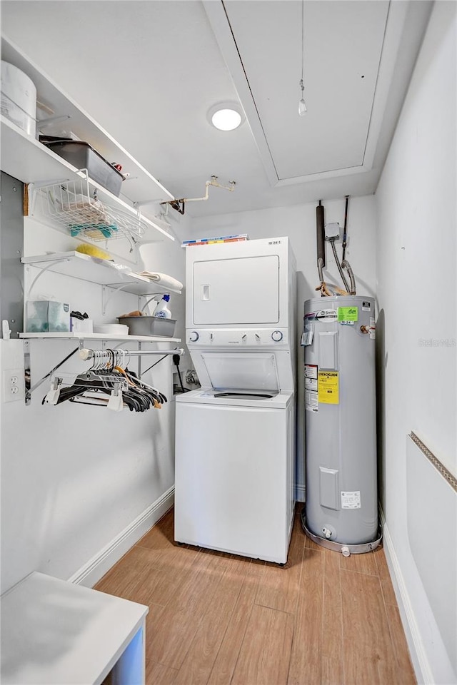 laundry room featuring laundry area, stacked washer / dryer, water heater, light wood-type flooring, and attic access