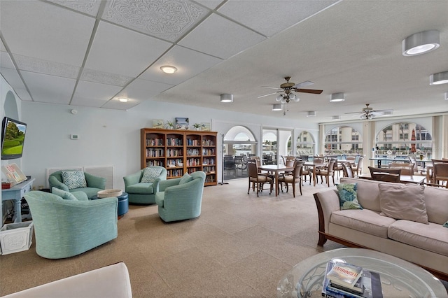 living room with light floors, a ceiling fan, and a drop ceiling