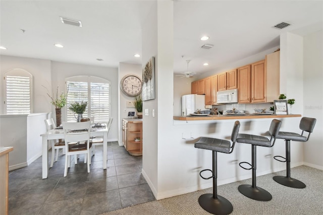 kitchen with white appliances, visible vents, decorative backsplash, a peninsula, and a kitchen bar