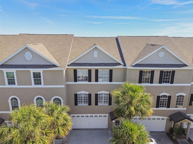 townhome / multi-family property featuring a garage, concrete driveway, roof with shingles, and stucco siding