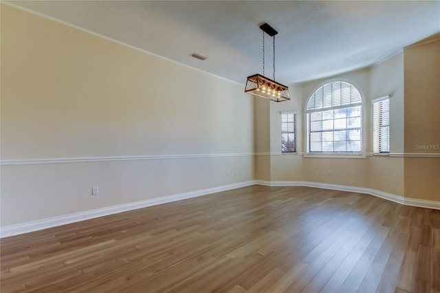 empty room with baseboards, wood finished floors, visible vents, and a notable chandelier