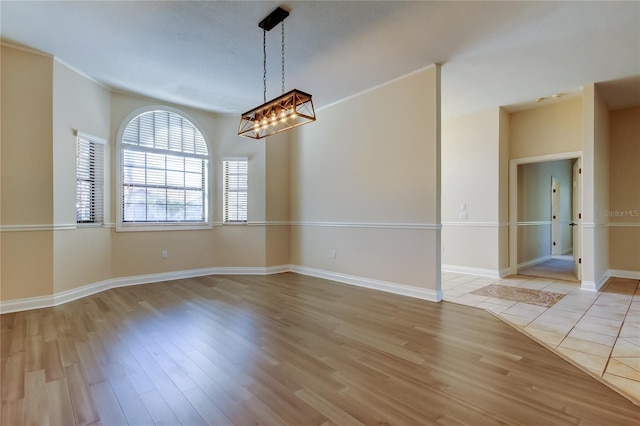spare room featuring light wood finished floors, an inviting chandelier, and baseboards