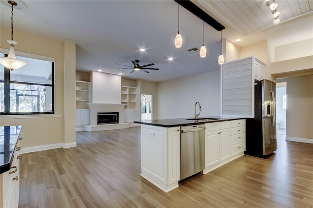 kitchen featuring stainless steel appliances, dark countertops, light wood-style floors, a glass covered fireplace, and a sink
