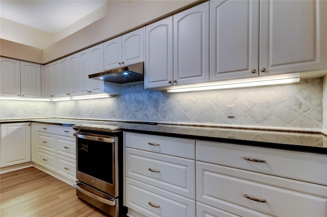 kitchen featuring electric stove, light wood finished floors, dark countertops, white cabinets, and under cabinet range hood