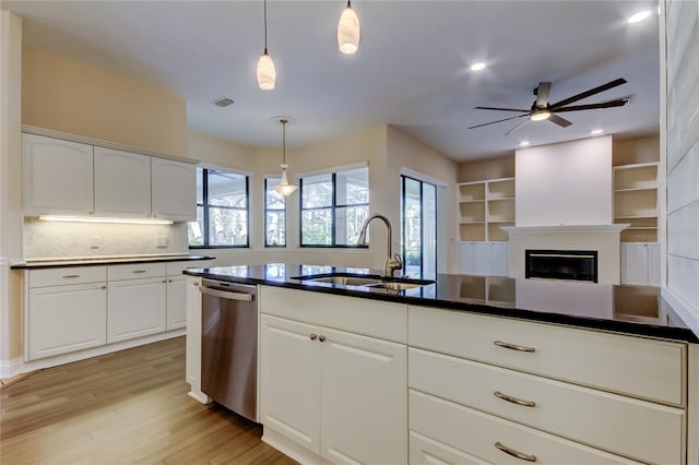 kitchen with light wood finished floors, dark countertops, visible vents, stainless steel dishwasher, and a sink