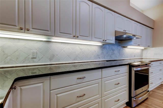 kitchen with dark countertops, under cabinet range hood, tasteful backsplash, and white cabinets