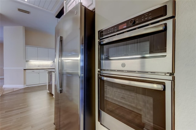 kitchen featuring stainless steel appliances, visible vents, white cabinetry, light wood finished floors, and tasteful backsplash