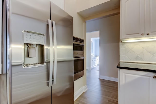 kitchen featuring stainless steel appliances, dark countertops, white cabinetry, and tasteful backsplash