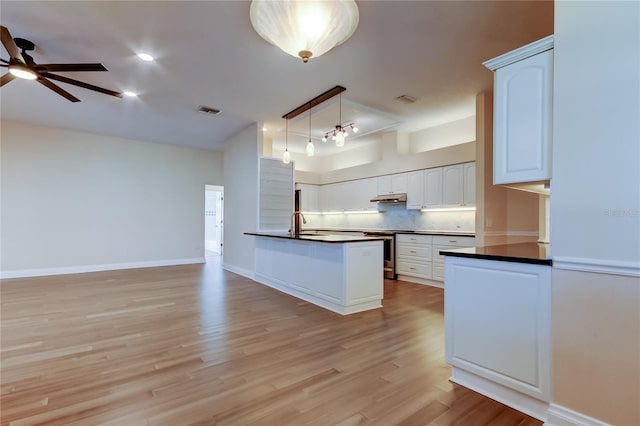 kitchen with dark countertops, visible vents, backsplash, light wood-style floors, and under cabinet range hood