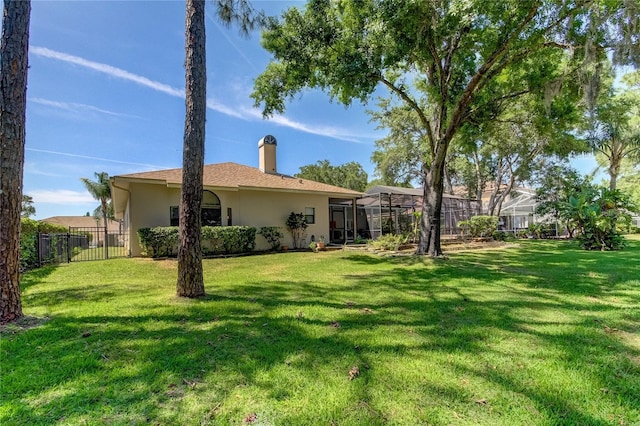 rear view of house featuring glass enclosure, fence, a lawn, and stucco siding