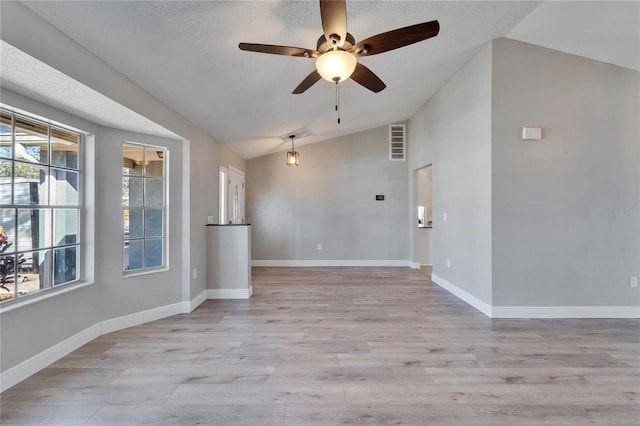 spare room with visible vents, light wood-style flooring, vaulted ceiling, a textured ceiling, and baseboards