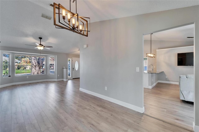 unfurnished living room featuring visible vents, lofted ceiling, a textured ceiling, light wood-style floors, and ceiling fan with notable chandelier