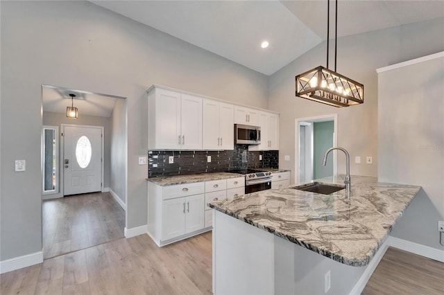 kitchen with decorative light fixtures, stainless steel appliances, white cabinets, a sink, and a peninsula