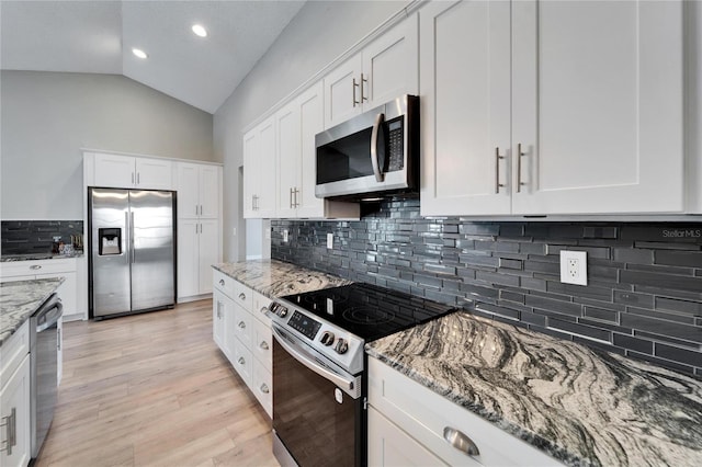 kitchen featuring white cabinets, appliances with stainless steel finishes, light stone counters, vaulted ceiling, and light wood-type flooring