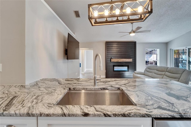 kitchen featuring a fireplace, visible vents, open floor plan, a sink, and a textured ceiling