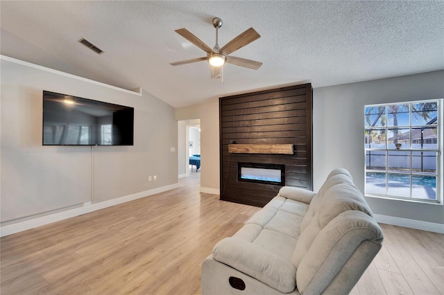 living room featuring a textured ceiling, light wood-style flooring, a fireplace, visible vents, and vaulted ceiling