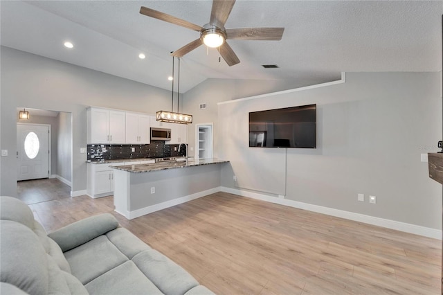 kitchen featuring stainless steel microwave, hanging light fixtures, open floor plan, white cabinets, and a peninsula