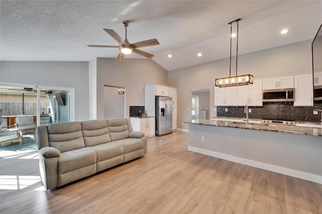 living area featuring ceiling fan, high vaulted ceiling, a textured ceiling, baseboards, and light wood-type flooring