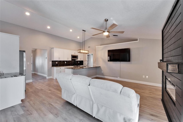 living room featuring lofted ceiling, a textured ceiling, light wood-type flooring, and a ceiling fan