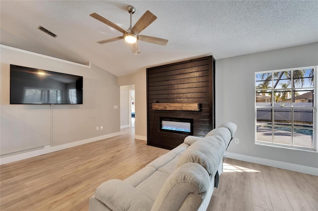 living area with a fireplace, lofted ceiling, visible vents, light wood-style flooring, and a textured ceiling