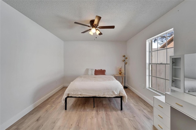 bedroom with light wood finished floors, baseboards, and a textured ceiling