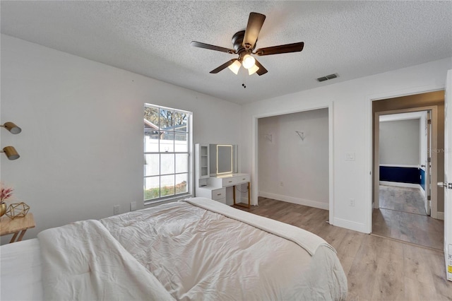 bedroom with a textured ceiling, ceiling fan, visible vents, baseboards, and light wood-style floors