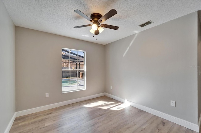 empty room with light wood finished floors, baseboards, visible vents, and a textured ceiling