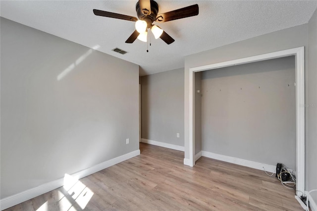 unfurnished bedroom featuring visible vents, baseboards, light wood-style flooring, ceiling fan, and a textured ceiling