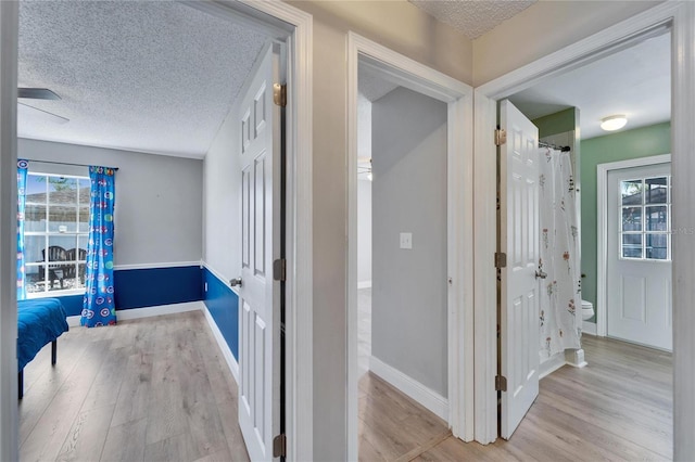 corridor featuring light wood-type flooring, baseboards, and a textured ceiling