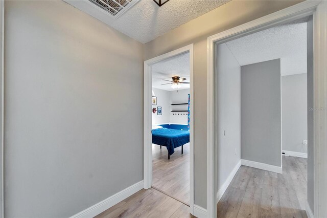 hallway with a textured ceiling, visible vents, light wood-style flooring, and baseboards