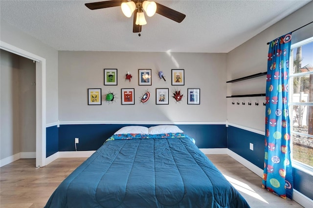 bedroom with a ceiling fan, baseboards, a textured ceiling, and light wood finished floors