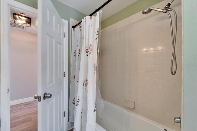 bathroom featuring wood finished floors, shower / bath combination with curtain, and baseboards