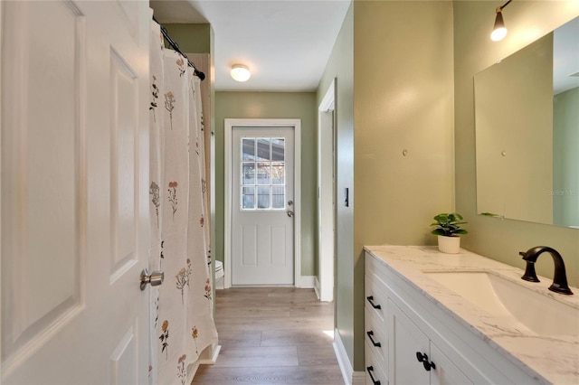 bathroom featuring toilet, baseboards, wood finished floors, and vanity