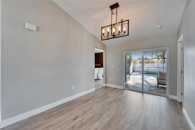 unfurnished room featuring light wood-style flooring, a chandelier, vaulted ceiling, and baseboards