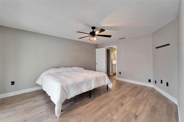 bedroom with light wood-style floors, visible vents, baseboards, and a textured ceiling