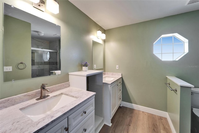 bathroom with wood finished floors, two vanities, a sink, baseboards, and a stall shower