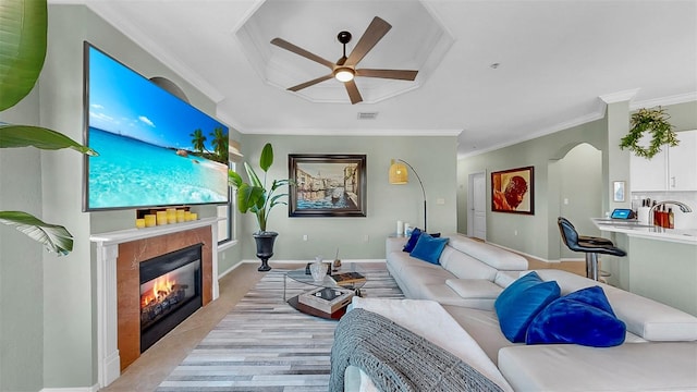 living room with crown molding, baseboards, arched walkways, and a tiled fireplace