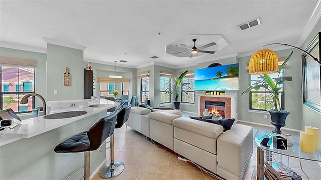 living area with light tile patterned floors, visible vents, ornamental molding, a glass covered fireplace, and a textured ceiling