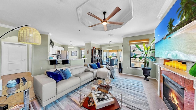 living room with a textured ceiling, ceiling fan, ornamental molding, and a tiled fireplace