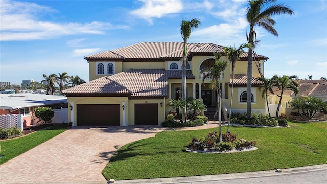 mediterranean / spanish-style house featuring a garage, a tiled roof, decorative driveway, a front lawn, and stucco siding