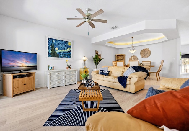 living room with a ceiling fan, a tray ceiling, baseboards, and light wood finished floors