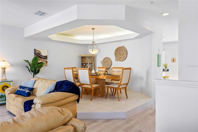 dining space with baseboards, visible vents, a tray ceiling, and wood finished floors