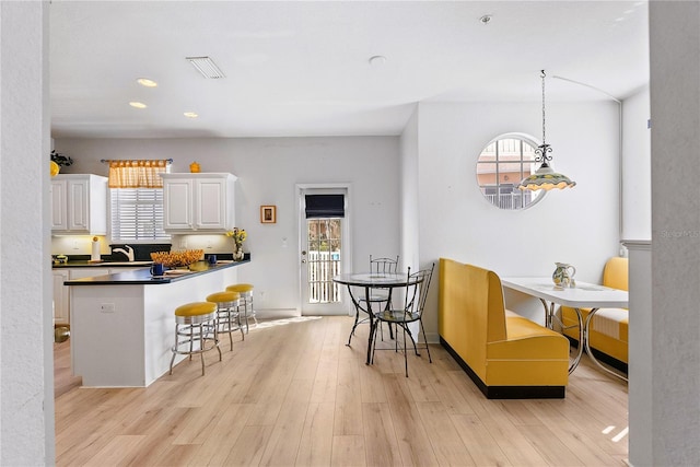 kitchen with a breakfast bar, light wood finished floors, visible vents, white cabinets, and a sink