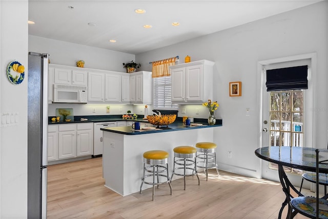 kitchen with a breakfast bar area, dark countertops, white microwave, freestanding refrigerator, and white cabinetry