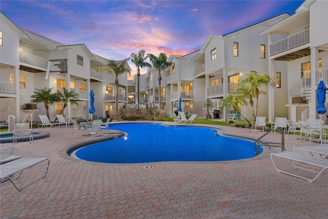 pool at dusk with a residential view, a patio, and a community pool